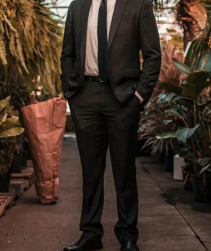 man wearing suit jacket standing between the plants